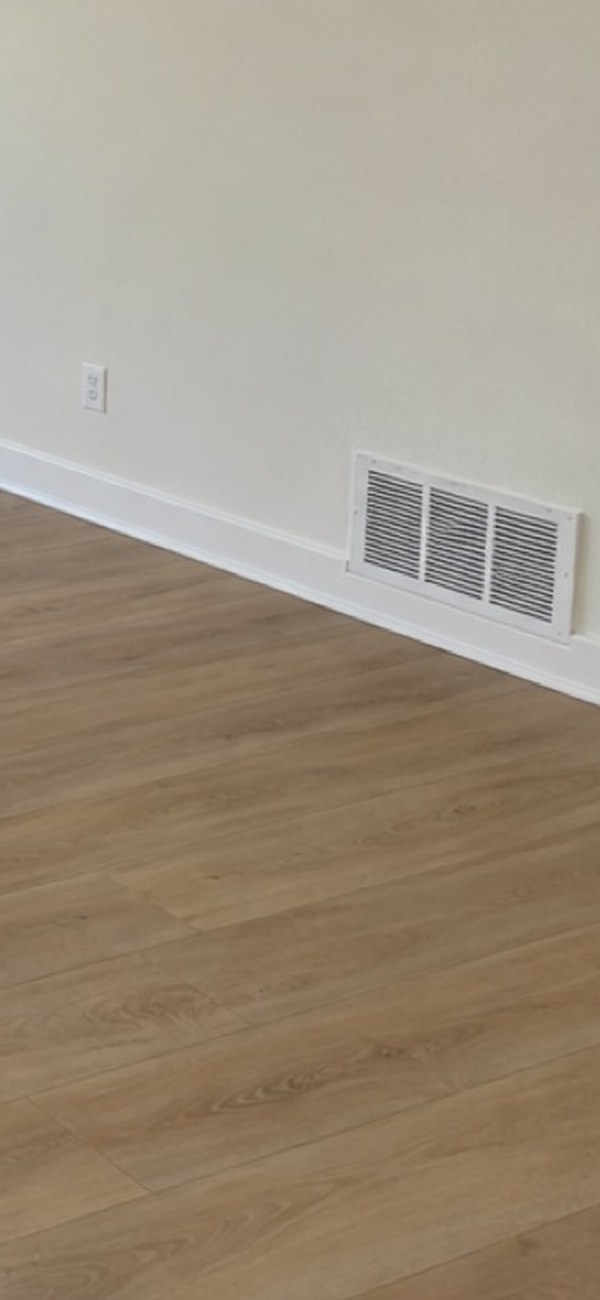 The borrower's second draw photo of the same room, angled down onto the new wood flooring where it meets the painted baseboard and the return-air vent.